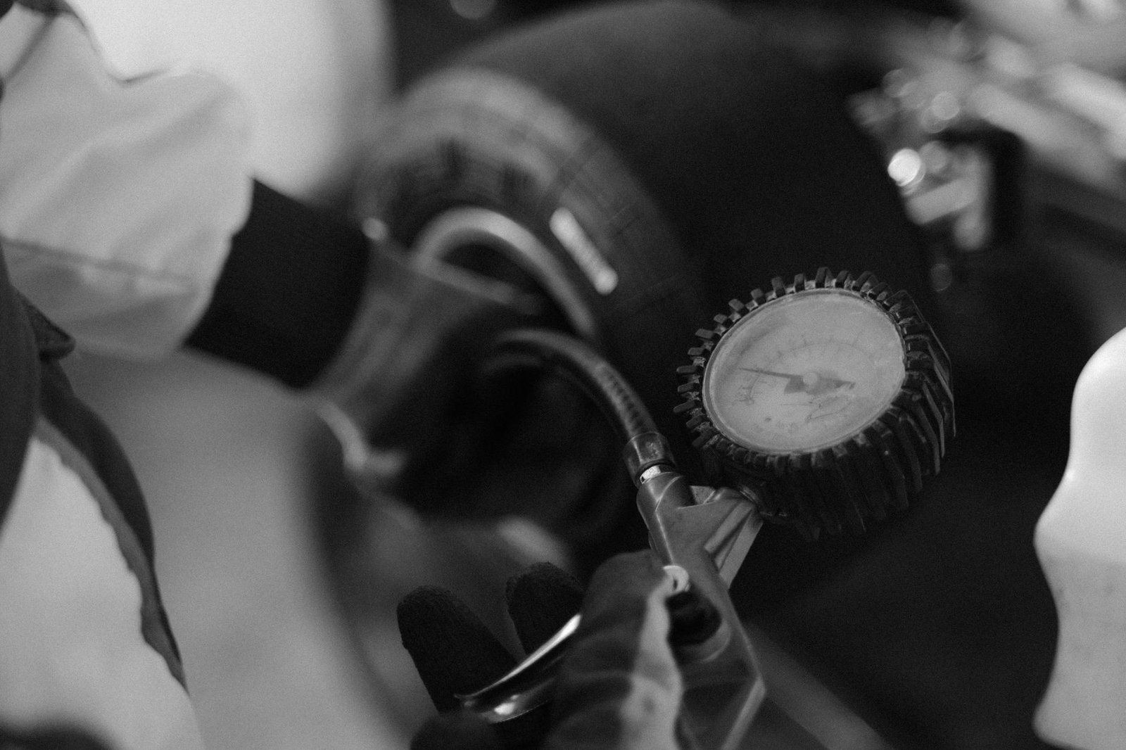 A professional analog tire pressure gauge sits on the asphalt at a racetrack.
